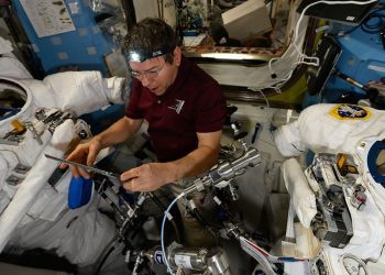 El astronauta Mike Barratt lee los procedimientos de mantenimiento mientras trabaja en un par de trajes espaciales dentro de la esclusa de aire Quest.